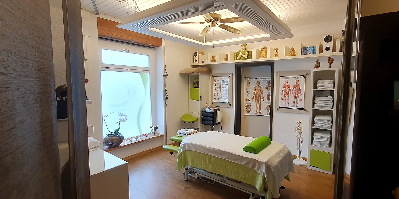 Behandlungsraum der PlusPraxis mit Massageliege, hellem Holzboden und grünen Akzenten